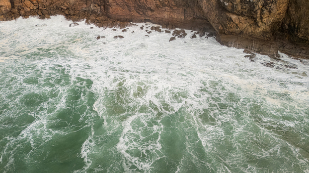 Aerial view of rough turquoise waves crashing against the rugged limestone cliffs with white sea foam Sagres Faro Portugal. Aerial view of rough turquoise waves crashing against the rugged limestone cliffs with white sea foam Sagres Faro Portugal.