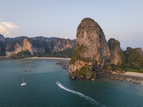 Aerial view of a speedboat zipping across turquoise waters towards towering cliffs and pristine beaches Krabi Thailand.
