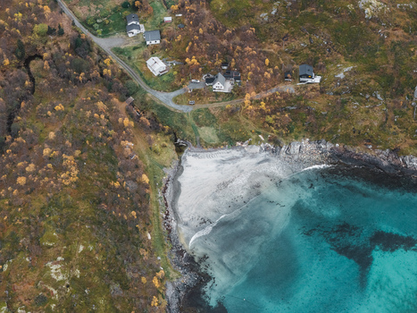 Aerial view of the rugged coastline of Senja featuring a small sandy beach turquoise waters and scattered houses nestled among autumn colored hills in Senja Troms Norway.
