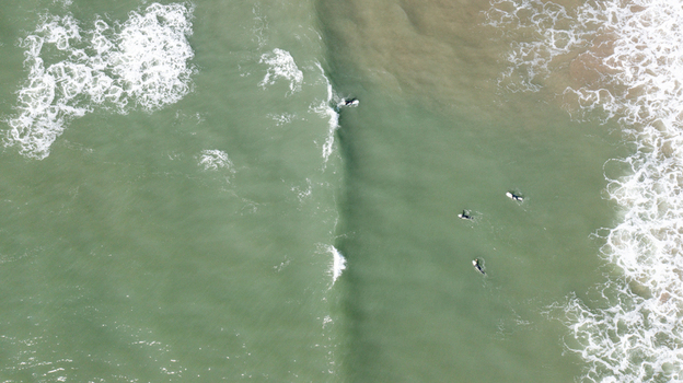 Aerial view of surfers floating in the greenish sea water with white foam waves at Bantham Beach in Kingsbridge Devon United Kingdom. Aerial view of surfers floating in the greenish sea water with white foam waves at Bantham Beach in Kingsbridge Devon United Kingdom.