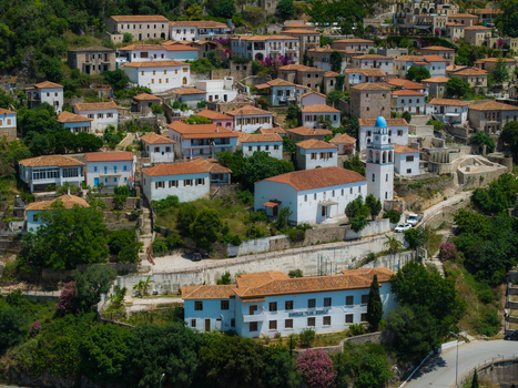 Aerial view of the historic village with traditional white houses terracotta roofs and a blue domed church nestled on a hillside with lush greenery Dhermi Vlore County Albania. Aerial view of the historic village with traditional white houses terracotta roofs and a blue domed church nestled on a hillside with lush greenery Dhermi Vlore County Albania.
