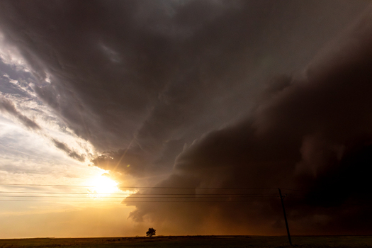 View of a dramatic supercell storm cloud formation at sunset over the flat plains with power lines and a solitary tree in the foreground in Oklahoma City Oklahoma United States.