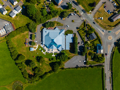 Aerial view of a building with a complex roof and glass atrium surrounded by parking lots and green fields in Rocroi Grand Est France. Aerial view of a building with a complex roof and glass atrium surrounded by parking lots and green fields in Rocroi Grand Est France.