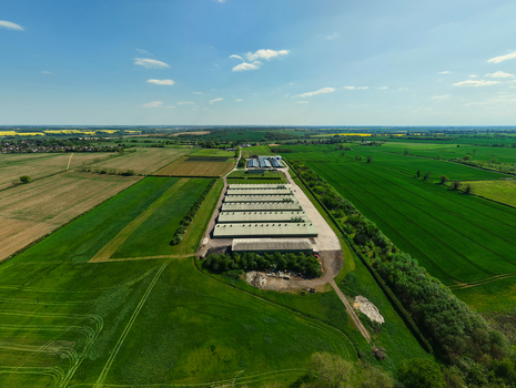 Aerial view of a large agricultural facility with long green roofed buildings surrounded by lush green fields and farmland under a blue sky Kettering England United Kingdom. Aerial view of a large agricultural facility with long green roofed buildings surrounded by lush green fields and farmland under a blue sky Kettering England United Kingdom.