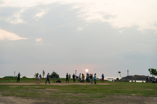 View of people playing cricket on a green field by the ocean during a golden sunset Galle Southern Province Sri Lanka.