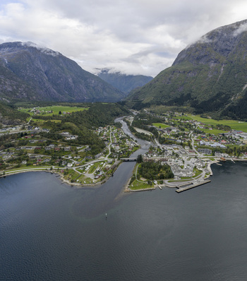 Aerial view of the village of Eidfjord nestled between steep mountains and the fjord with a river flowing through the valley under a cloudy sky Eidfjord Vestland Norway. Aerial view of the village of Eidfjord nestled between steep mountains and the fjord with a river flowing through the valley under a cloudy sky Eidfjord Vestland Norway.