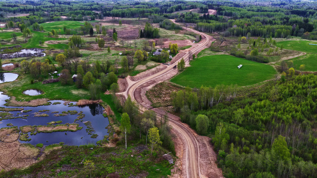 Aerial view of a dirt access road winding through a rural landscape with green fields forests and small ponds in Latvija. Aerial view of a dirt access road winding through a rural landscape with green fields forests and small ponds in Latvija.