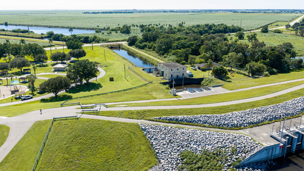 Aerial view of the Pahokee Marina area featuring a canal a small utility building lush green parkland and expansive agricultural fields in Pahokee Florida United States. Aerial view of the Pahokee Marina area featuring a canal a small utility building lush green parkland and expansive agricultural fields in Pahokee Florida United States.