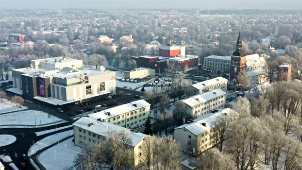 Aerial view of a snow covered town featuring a historic church with a tall spire modern buildings and residential blocks surrounded by frost covered trees in Latvija. Aerial view of a snow covered town featuring a historic church with a tall spire modern buildings and residential blocks surrounded by frost covered trees in Latvija.