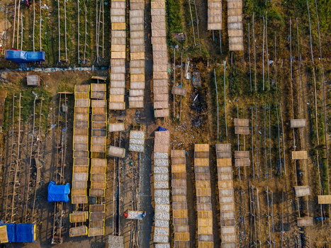 Aerial view of numerous wooden racks used for drying fish arranged in neat rows on the ground with blue tarps and rural terrain in Cilacap Regency Central Java Indonesia. Aerial view of numerous wooden racks used for drying fish arranged in neat rows on the ground with blue tarps and rural terrain in Cilacap Regency Central Java Indonesia.