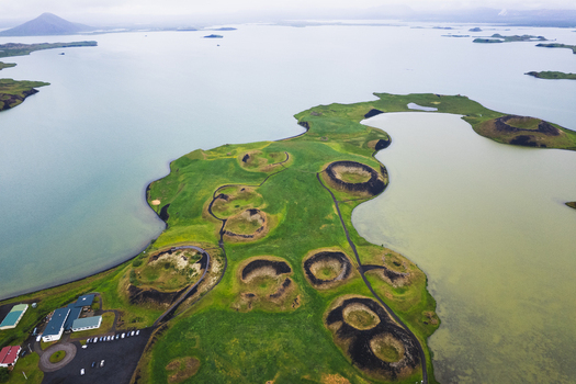 Aerial view of the verdant pseudo craters dotting the landscape contrast starkly with the surrounding serene waters of Skutustadagigar Lake Myvatn Iceland.