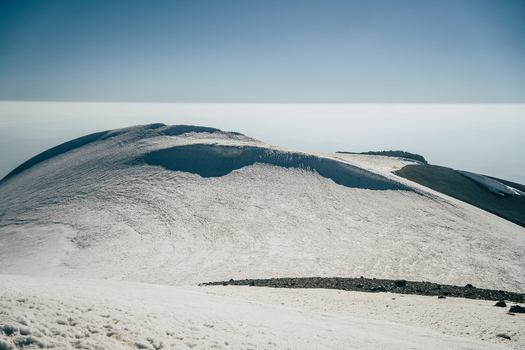 View of the snow covered peak of Mount Ararat with rocky slopes under a clear blue sky in Turkey.