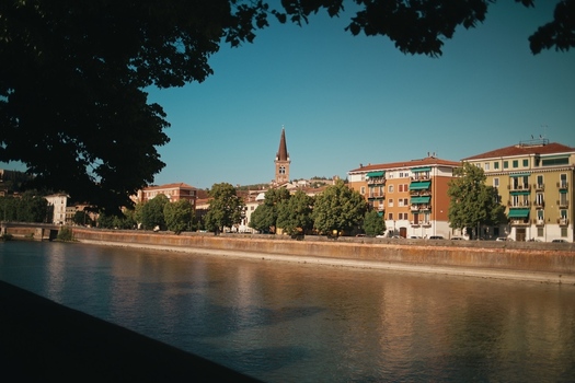 View of the Adige river waterfront with colorful historic buildings and a church steeple under a clear blue sky in Verona Veneto Italy.