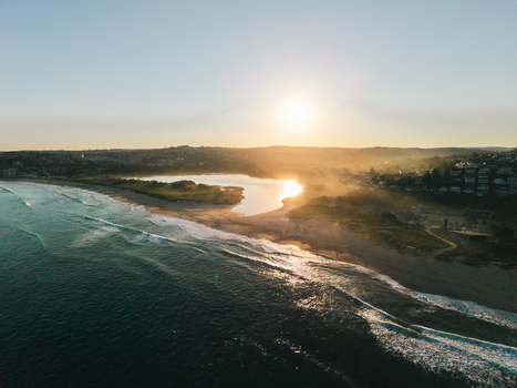 Aerial view of Dee Why Lagoon and beach at sunrise with golden light reflecting on the water and waves crashing on the shore in Dee Why New South Wales Australia. Aerial view of Dee Why Lagoon and beach at sunrise with golden light reflecting on the water and waves crashing on the shore in Dee Why New South Wales Australia.