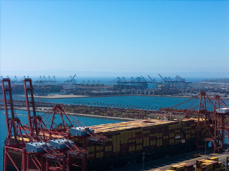 Aerial view of the Port of Long Beach featuring large container ships red gantry cranes and stacks of cargo containers under a clear blue sky in Long Beach California United States. Aerial view of the Port of Long Beach featuring large container ships red gantry cranes and stacks of cargo containers under a clear blue sky in Long Beach California United States.