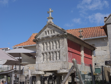 View of a traditional stone horreo with red wooden panels and a cross on top situated in the historic village of Combarro Pontevedra Spain.