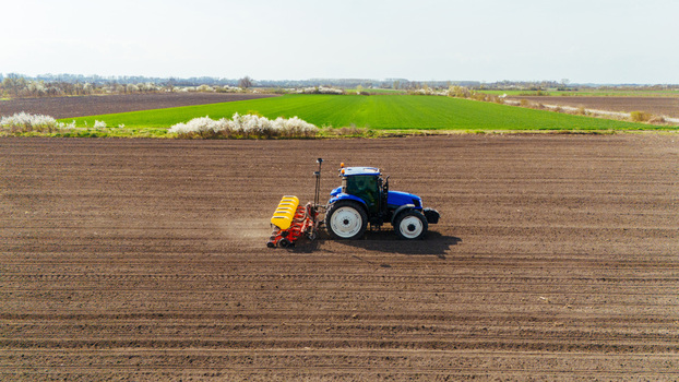 Aerial view of a blue tractor plowing lines in the brown earth contrasting with green fields under a pale sky Sremska Mitrovica Vojvodina Serbia. Aerial view of a blue tractor plowing lines in the brown earth contrasting with green fields under a pale sky Sremska Mitrovica Vojvodina Serbia.