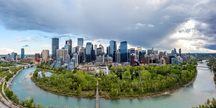 Aerial view of the Calgary skyline rising above the Bow River and lush greenery of Prince s Island Park under a dramatic cloudy sky in Calgary Alberta Canada.