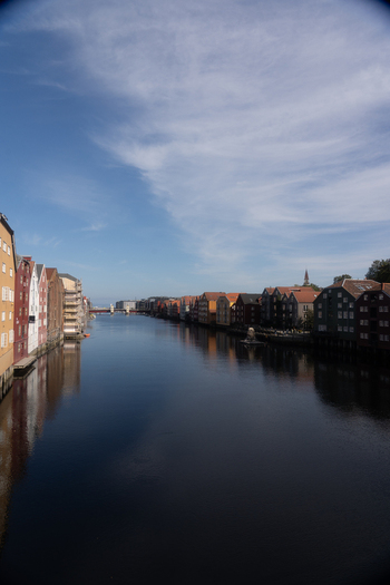 View of colorful historic wooden wharves reflecting in the calm waters of the Nidelva river under a blue sky in Trondheim Trondelag Norway. View of colorful historic wooden wharves reflecting in the calm waters of the Nidelva river under a blue sky in Trondheim Trondelag Norway.