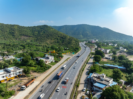Aerial view of a multi lane highway with cars and trucks winding through green hills and residential buildings in Udaipur Rajasthan India. Aerial view of a multi lane highway with cars and trucks winding through green hills and residential buildings in Udaipur Rajasthan India.