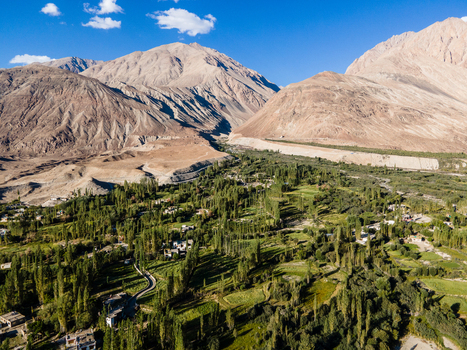 Aerial view of a lush green valley with trees and small buildings nestled among arid rocky mountains under a clear blue sky in Ladakh Ladakh India. Aerial view of a lush green valley with trees and small buildings nestled among arid rocky mountains under a clear blue sky in Ladakh Ladakh India.