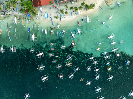 Aerial view of Naked Island featuring numerous traditional outrigger boats anchored in the clear turquoise and deep blue shallow waters near a sandy coastline in Siargao Philippines. Aerial view of Naked Island featuring numerous traditional outrigger boats anchored in the clear turquoise and deep blue shallow waters near a sandy coastline in Siargao Philippines.