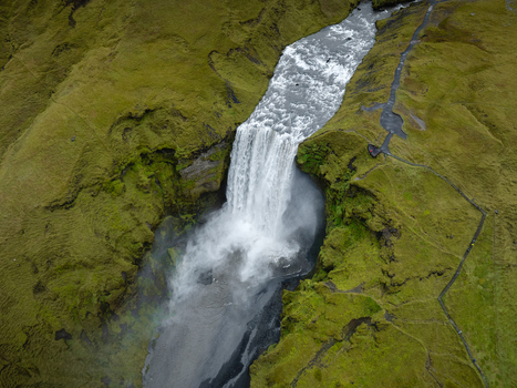 Aerial view of Skógafoss waterfall cascading down rugged cliffs into the river below surrounded by verdant green moss Skógafoss Rangárþing eystra Iceland. Aerial view of Skógafoss waterfall cascading down rugged cliffs into the river below surrounded by verdant green moss Skógafoss Rangárþing eystra Iceland.