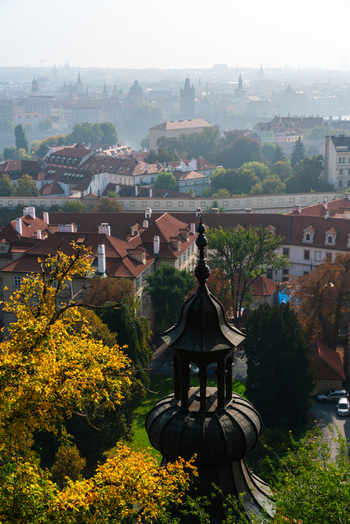View of the historic city skyline with red tiled rooftops a prominent dark church tower in the foreground and autumn foliage in Prague Prague Czechia.