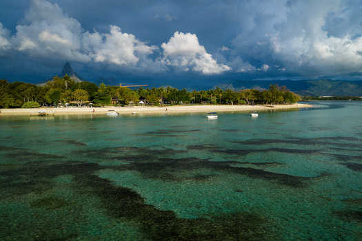 Aerial view of the turquoise lagoon and white sandy beach lined with palm trees and lush vegetation under a dramatic sky in Moka District Mauritius. Aerial view of the turquoise lagoon and white sandy beach lined with palm trees and lush vegetation under a dramatic sky in Moka District Mauritius.
