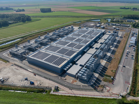 Aerial view of a large modern datacenter with extensive rooftop solar panels and cooling infrastructure surrounded by green agricultural fields in The Netherlands. Aerial view of a large modern datacenter with extensive rooftop solar panels and cooling infrastructure surrounded by green agricultural fields in The Netherlands.
