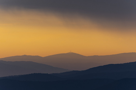View of layered mountain silhouettes fading into the golden sky a distant peak crowned with a structure casting long shadows in Brandlalm Styria Austria. View of layered mountain silhouettes fading into the golden sky a distant peak crowned with a structure casting long shadows in Brandlalm Styria Austria.