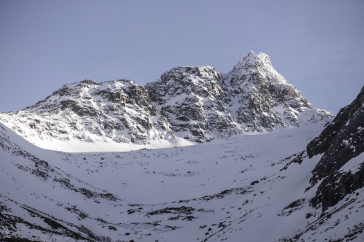 View of snow capped mountain peaks and rugged slopes under a clear blue sky in Kvaloya Troms Norway. View of snow capped mountain peaks and rugged slopes under a clear blue sky in Kvaloya Troms Norway.
