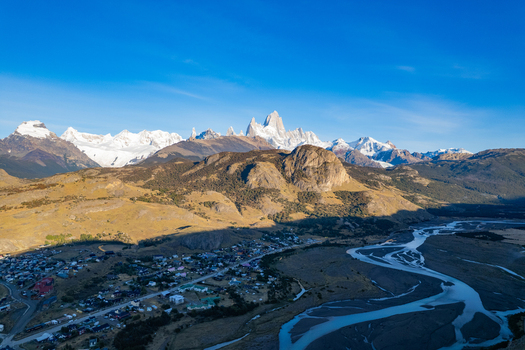 Aerial view of El Chalten nestled in the Patagonian landscape with snow capped peaks of Mount Fitz Roy in the background under a clear blue sky El Chalten Santa Cruz Argentina. Aerial view of El Chalten nestled in the Patagonian landscape with snow capped peaks of Mount Fitz Roy in the background under a clear blue sky El Chalten Santa Cruz Argentina.