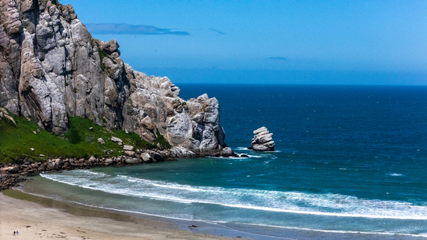 Aerial view of Morro Rock rising above the sandy beach and blue Pacific Ocean waves under a clear sky Morro Bay California United States.