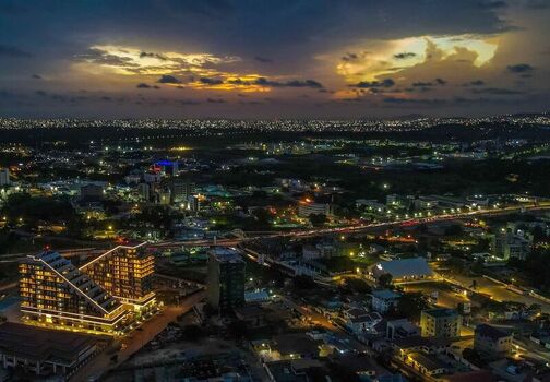 Aerial view of modern high rise buildings illuminated at night with city lights stretching across the horizon under a dramatic twilight sky in Ghana. Aerial view of modern high rise buildings illuminated at night with city lights stretching across the horizon under a dramatic twilight sky in Ghana.