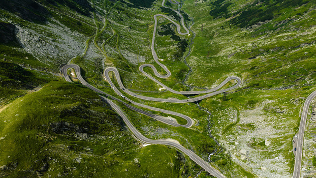 Aerial view of the winding Transfagarasan mountain road with sharp hairpin turns cutting through the lush green slopes of the Carpathian Mountains in Curtea de Arges Judetul Arges Romania.