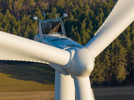 Aerial view of a wind turbine nacelle and blades with a forest and field in the background in Poland. Aerial view of a wind turbine nacelle and blades with a forest and field in the background in Poland.