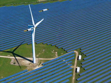 Aerial view of the Chelveston Wind Farm featuring rows of blue solar panels and a tall white wind turbine on a sunny day in Wellingborough England United Kingdom. Aerial view of the Chelveston Wind Farm featuring rows of blue solar panels and a tall white wind turbine on a sunny day in Wellingborough England United Kingdom.