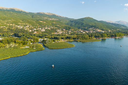 Aerial view of Lake Ohrid with a small boat on the blue water surrounded by lush green hills coastal reeds and a clear sky in Ohrid Municipality of Ohrid North Macedonia.