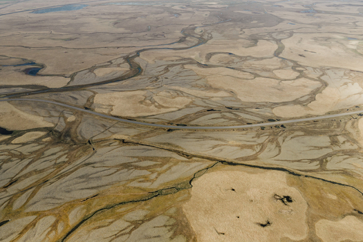 Aerial view of braided river channels cutting through the vast arid landscape with a road winding through the terrain in Hofn Sveitarfelagid Hornaf Iceland.