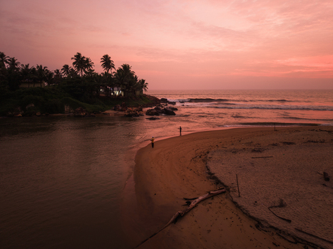 Aerial view of fishermen standing on a sandy beach at sunset with palm trees and ocean waves under a pink sky in Galle Southern Province Sri Lanka. Aerial view of fishermen standing on a sandy beach at sunset with palm trees and ocean waves under a pink sky in Galle Southern Province Sri Lanka.