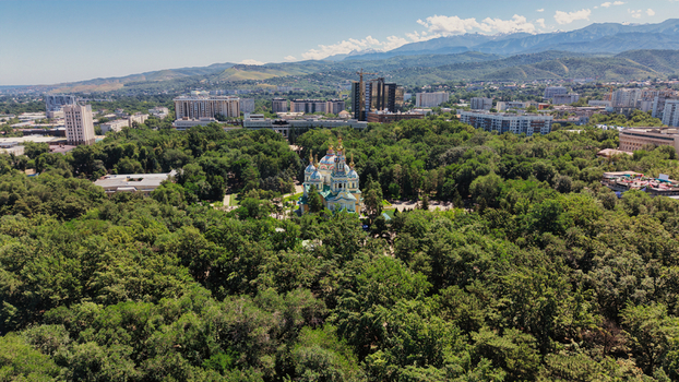 Aerial view of the Ascension Cathedral in the lush greenery of 28 Panfilov Guardsmen Park with the urban skyline and mountains in the background in Almaty Almaty Region Kazakhstan.