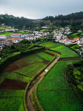 Aerial view of vibrant green fields contrasting with the red roofed houses nestled among the hills a winding road cutting through the landscape Furnas Azores Portugal.