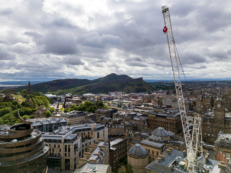 Aerial view of the historic city skyline of Edinburgh featuring Arthur s Seat and a construction crane rising above the urban architecture in Edinburgh Scotland United Kingdom.