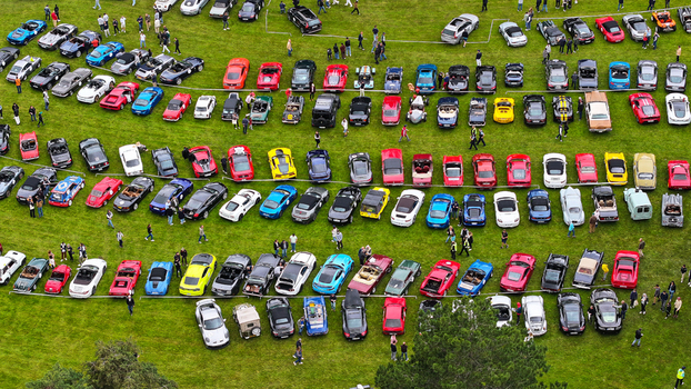 La Chapelle de Guinchay France 01 June 2024 Aerial view of rows of colorful sports cars and classic vehicles parked on a lush green field with people walking between them.