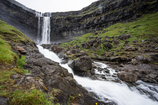View of a waterfall cascading down a rocky cliffside surrounded by lush green slopes in the Faroe Islands.