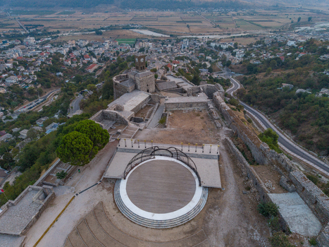 Aerial view of Gjirokaster Fortress featuring its historic clock tower stone fortifications and a circular stage area overlooking the city rooftops in Gjirokaster Gjirokaster County Albania. Aerial view of Gjirokaster Fortress featuring its historic clock tower stone fortifications and a circular stage area overlooking the city rooftops in Gjirokaster Gjirokaster County Albania.