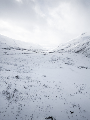 Aerial view of a vast snowy valley nestled between mountain peaks under a cloudy sky in Ersfjord Troms Norway. Aerial view of a vast snowy valley nestled between mountain peaks under a cloudy sky in Ersfjord Troms Norway.