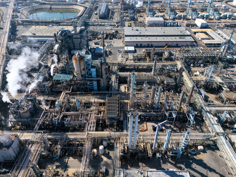 Aerial view of an industrial oil refinery in Carson featuring complex piping storage tanks tall distillation towers and smoke rising from a vent Carson California United States.