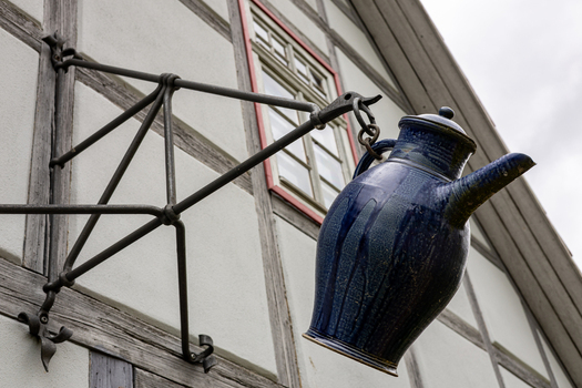 View of a blue ceramic pitcher hanging from a wrought iron sign bracket on a traditional half timbered house at the Hennebergisches Museum Kloster Vessra Thuringen Germany. View of a blue ceramic pitcher hanging from a wrought iron sign bracket on a traditional half timbered house at the Hennebergisches Museum Kloster Vessra Thuringen Germany.